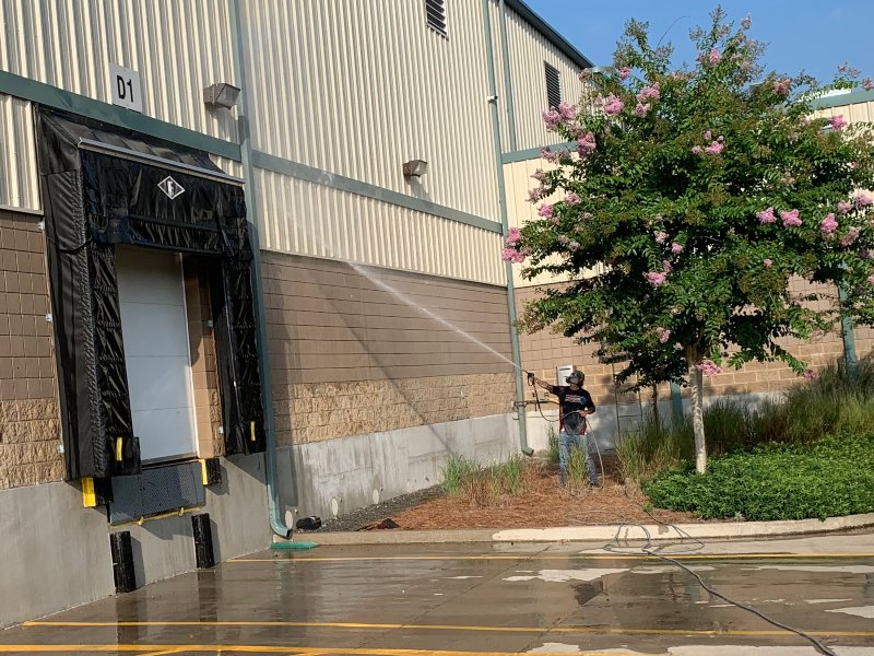 A Supreme Clean field agent pressure washing the siding on a commercial building