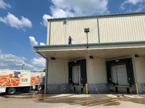 A service technician on the roof of Hunt Brothers Pizza soft washing a higher roof