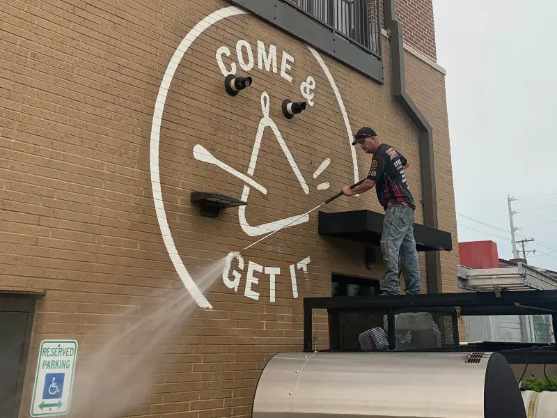 A service professional pressure washing the side of a brick commercial building