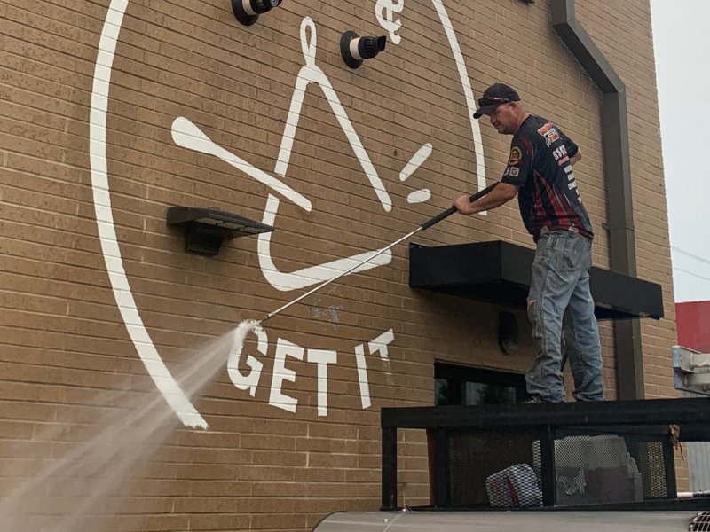 A service professional pressure washing the side of a brick commercial building