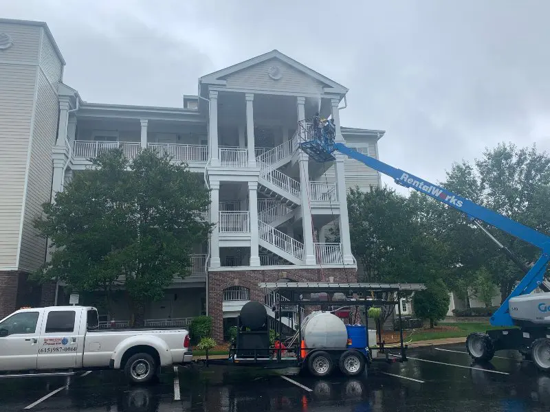 A service technician in a lift soft washing the roof of a commercial building