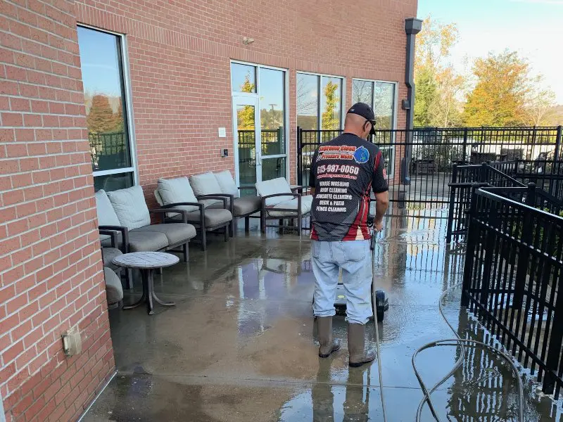 A Supreme Clean staff member washing the concrete lounge area of a commercial property