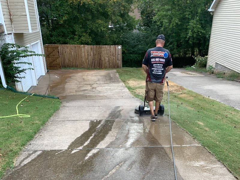A Supreme Clean staff member cleaning a wet and dirty concrete driveway