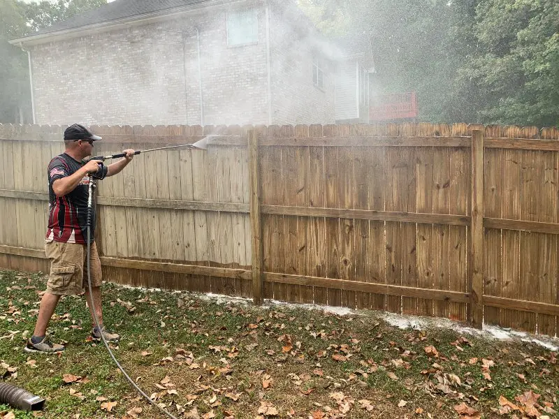 A Supreme Clean service agent in the middle of cleaning and staining a wooden fence
