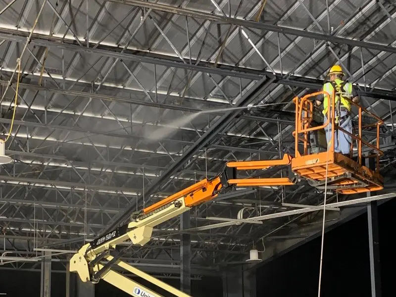 A professional technician in a lift soft washing support beams on a roof