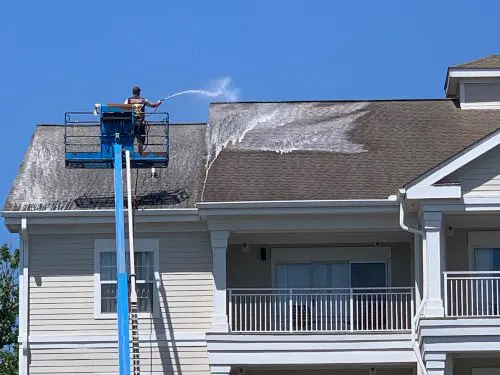 A Supreme Clean service professional in a lift soft washing a roof